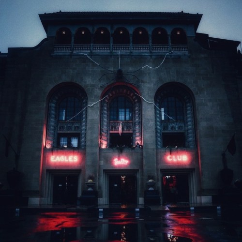 A historic building at night, featuring red neon signs for "Eagles Club" and reflections on wet pavement.