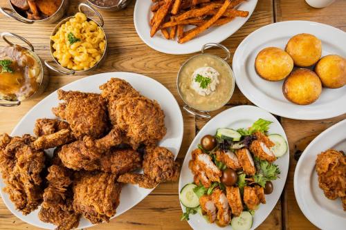 A spread of fried chicken, macaroni and cheese, cornbread, salad, and sweet potato fries on a wooden table.