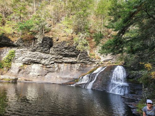 A serene waterfall cascades into a calm pool, surrounded by rocky cliffs and lush greenery.