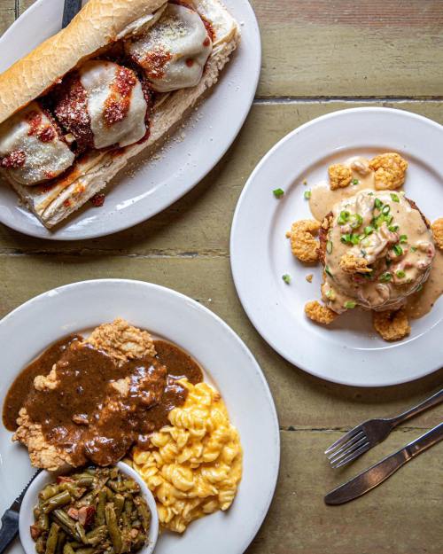 A plate of chicken with gravy, macaroni and cheese, and green beans, alongside a sandwich and a dish topped with sauce.