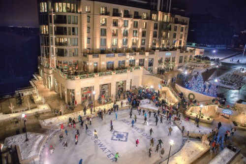 A bustling ice skating rink surrounded by a festive atmosphere and a beautifully lit building at night.