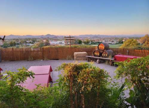 Scenic view of mountains at sunset, with picnic tables and barrels in a rustic outdoor setting.