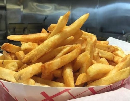 A close-up of a large serving of golden, crispy French fries in a red and white paper container.