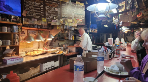 A busy diner with a counter, a chef cooking, and customers enjoying their meals in a cozy, rustic atmosphere.