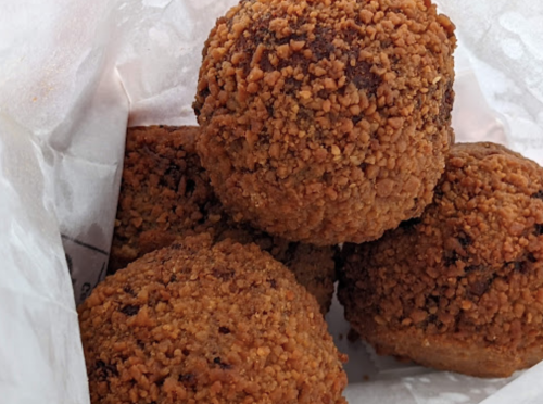 A close-up of four golden-brown, crunchy balls coated in crushed nuts, nestled in white paper.