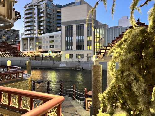 A serene waterfront scene at dusk, featuring buildings, a river, and decorative elements along the shore.