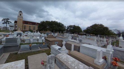 A panoramic view of a cemetery with numerous gravestones and a church in the background under a cloudy sky.