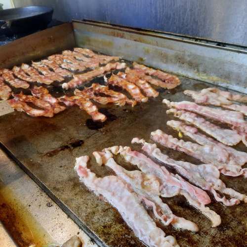 Sizzling strips of bacon cooking on a griddle, with some crispy and others still raw.