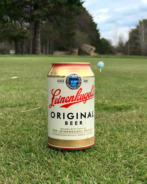 A can of Leinenkugel's Original Beer sits on green grass, with a golf ball and flag in the background.