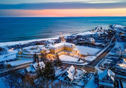 Aerial view of a snowy coastal town at sunset, featuring a large hotel and nearby houses along the shoreline.