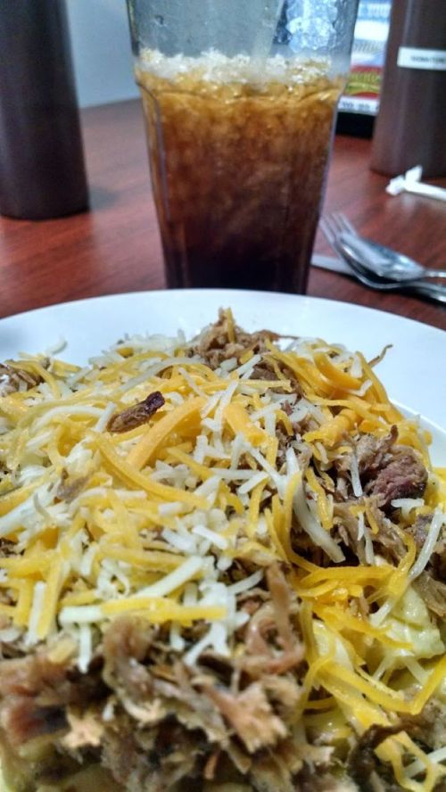 A plate of pasta topped with shredded meat and cheese, with a glass of iced drink in the background.