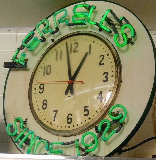 A round clock with neon green lettering reading "PERRELL'S SINCE 1920," showing the time as 10:10.