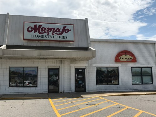 Exterior of Mama Jo's Homestyle Pies shop, featuring a sign and a pie logo on a sunny day.