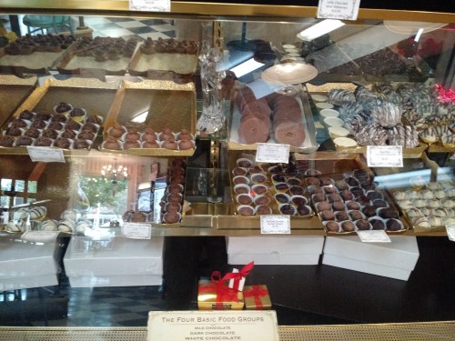 Display case filled with various chocolates and confections, labeled with names and prices.