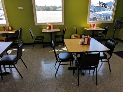 Interior of a casual dining area with empty tables, green walls, and large windows letting in natural light.