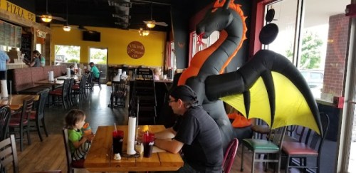 A child sits at a table in a restaurant, while a large inflatable dragon looms behind them.