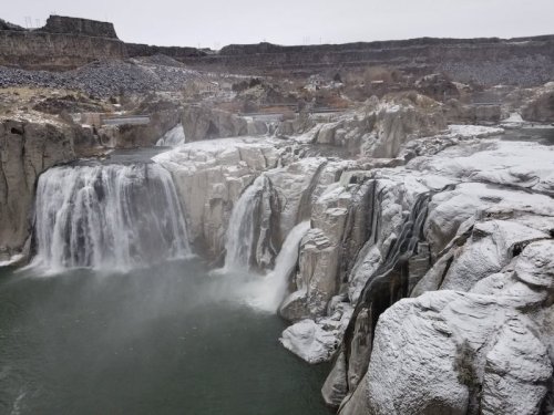 A scenic view of a waterfall cascading over rocky cliffs, surrounded by a misty atmosphere and icy terrain.