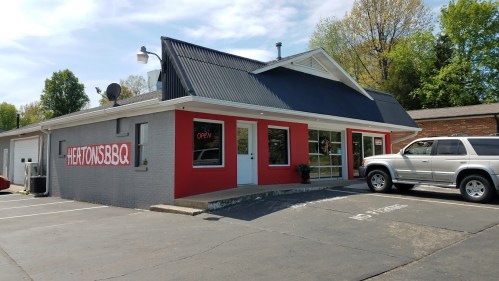 A BBQ restaurant with a red and gray exterior, large windows, and a parking lot, featuring an "Open" sign.