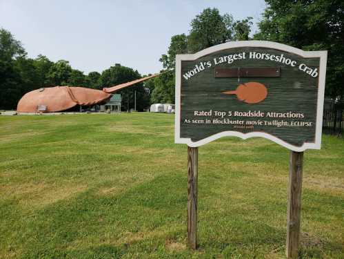 Sign for the world's largest horseshoe crab sculpture, with a grassy area and trees in the background.