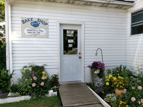 A quaint bake shop entrance with a sign, flowers, and a welcoming "OPEN" sign on the door.