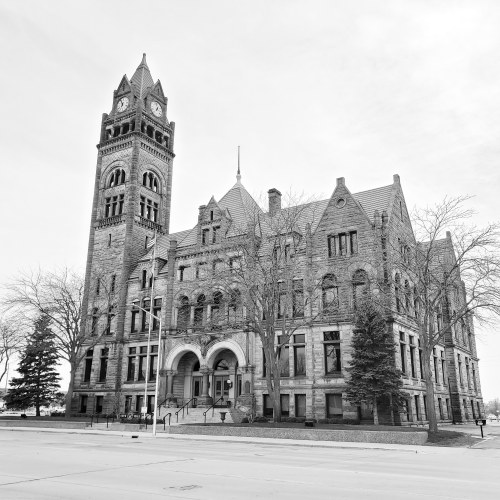 Historic stone building with a tall clock tower, surrounded by bare trees, in a black and white setting.