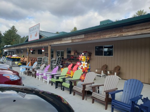A storefront with colorful Adirondack chairs outside, surrounded by garden supplies and a cloudy sky.