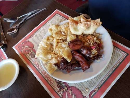 A plate of fried rice, crispy wontons, and glazed meat, served on a decorative placemat.