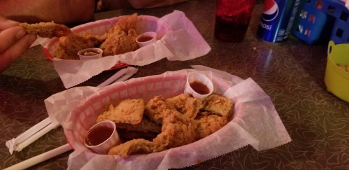 Two baskets of fried chicken with dipping sauce on a table, accompanied by drinks and utensils.