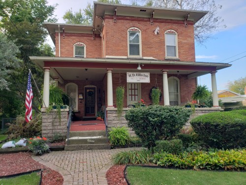 A brick house with a porch, American flag, and landscaped garden, featuring a sign that reads "H.D. Ellis Inn."
