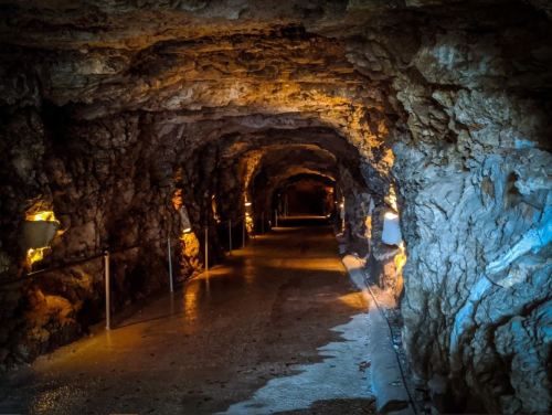A dimly lit cave tunnel with rocky walls and a smooth path, illuminated by soft lights along the sides.
