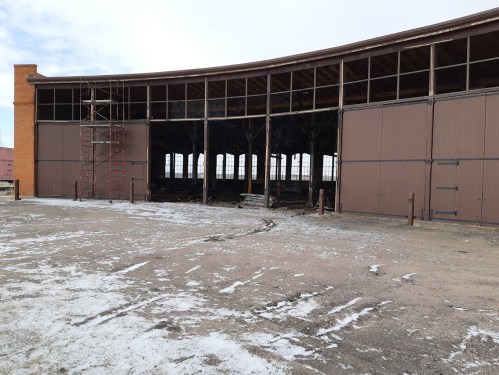 Abandoned building with large open doors, scaffolding, and snow-covered ground.