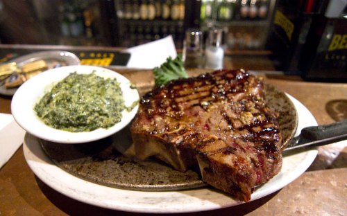 A grilled steak on a plate next to a bowl of creamed spinach, set on a wooden table in a restaurant.