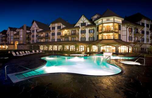 A beautifully lit hotel with a pool at night, featuring elegant architecture and lounge chairs around the water.