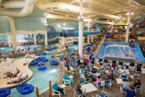 Indoor water park featuring slides, a wave pool, lazy river, and families enjoying the attractions and dining areas.
