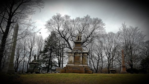 A somber cemetery scene with ornate gravestones and bare trees under a cloudy sky.