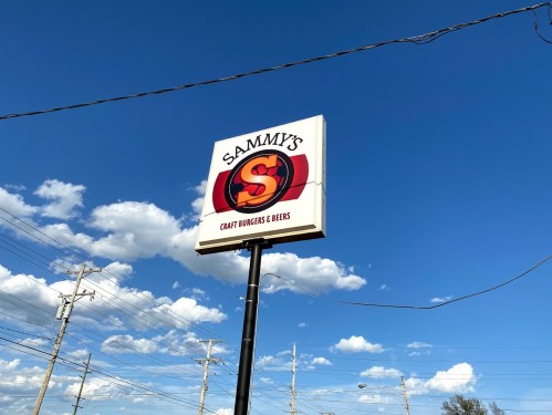 Sign for Sammy's Craft Burgers & Beers against a blue sky with clouds.