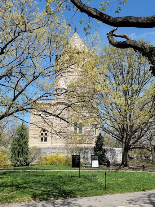 A stone tower surrounded by trees with budding leaves, set against a clear blue sky in a park.