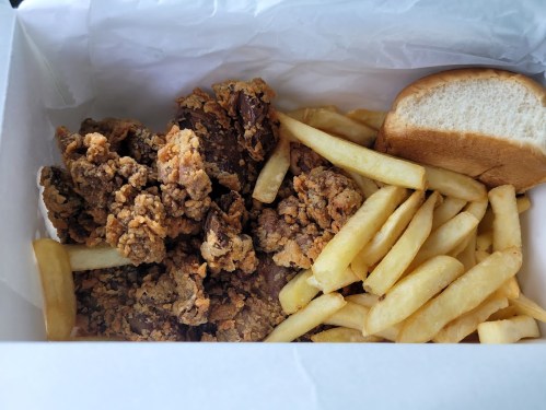 A takeout box containing fried chicken pieces, French fries, and a soft bread roll.