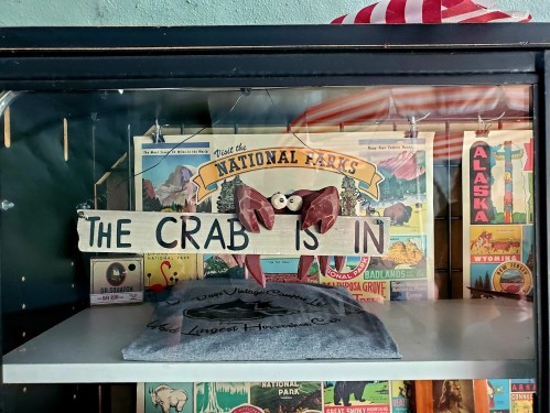 A sign reading "THE CRAB IS IN" with a crab decoration, displayed among vintage national park posters.
