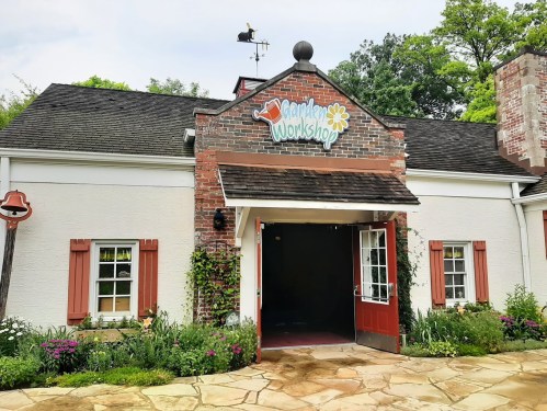 A charming building with a sign reading "Garden Workshop," surrounded by colorful flowers and greenery.