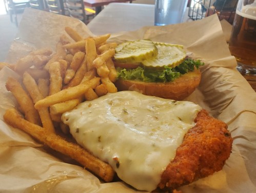 A plate of crispy fried chicken sandwich topped with pickles and lettuce, served with a side of golden fries.