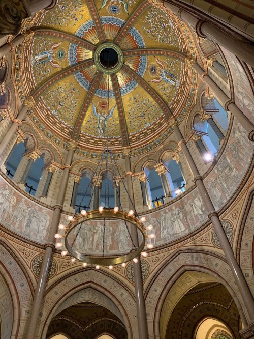 Intricate dome with vibrant gold and blue patterns, surrounded by ornate columns and a circular chandelier.