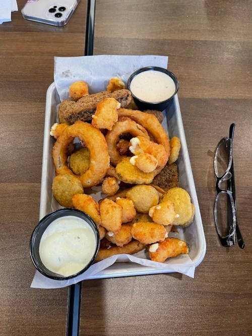 A metal tray filled with various fried foods, including onion rings, shrimp, and two dipping sauces.