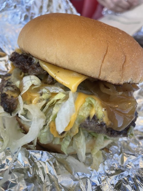 A close-up of a cheeseburger with lettuce, melted cheese, and a soft bun, wrapped in foil.