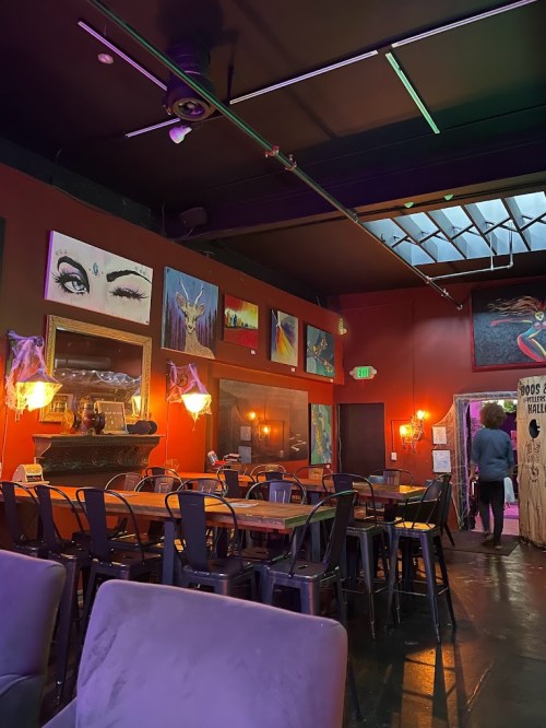 A vibrant restaurant interior with colorful artwork on the walls, wooden tables, and a person walking towards a doorway.