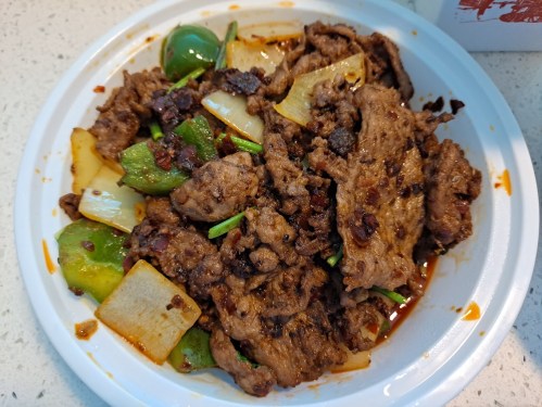 A bowl of stir-fried beef with green peppers and onions, garnished with herbs and a spicy sauce.