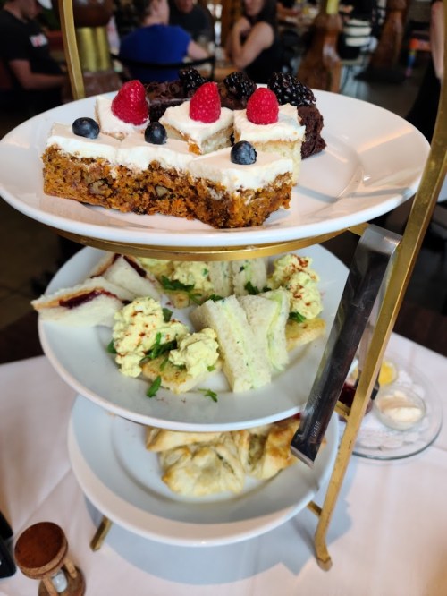 A tiered dessert stand featuring cake slices topped with berries, sandwiches, and pastries.