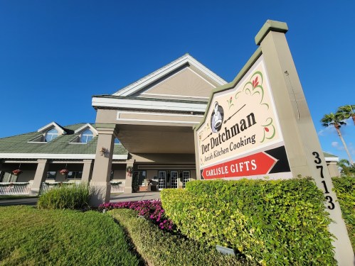 Sign for Der Dutchman restaurant and gift shop, featuring a welcoming entrance and colorful landscaping.