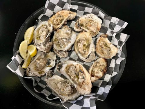 A platter of fresh oysters on a bed of checkered paper, garnished with lemon wedges.