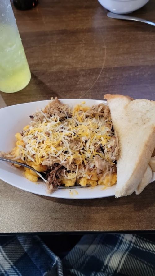 A bowl of macaroni and cheese topped with shredded meat and cheese, served with a slice of bread on the side.
